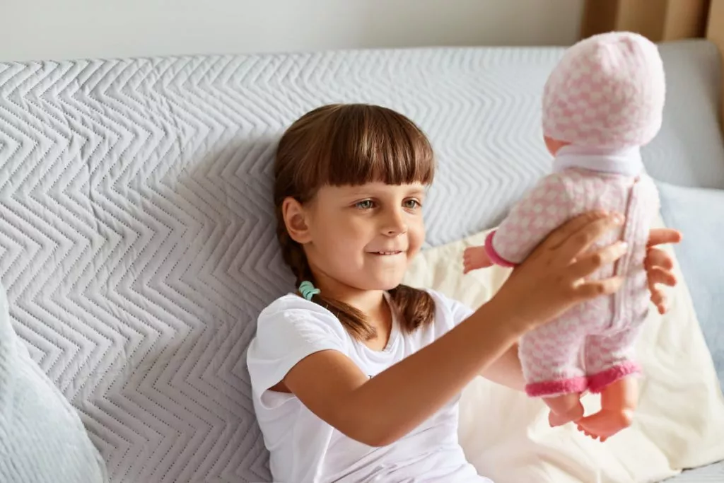 dark-haired-female-child-wearing-white-t-shirt-has-pigtails-raising-her-doll-looking-at-her-toy-with-smile-playing-alone-while-sitting-on-sofa-at-home.jpg